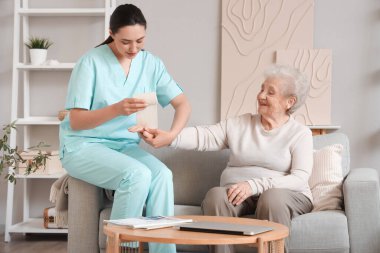 Kolunu evde bandajlayan fizyoterapist kıdemli bir kadın.