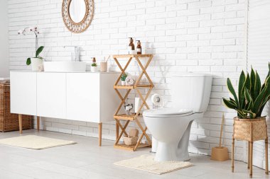 Beyaz klozet, raf ünitesi ve lavabolu çekmeceler tuvalette beyaz duvarın yanında.