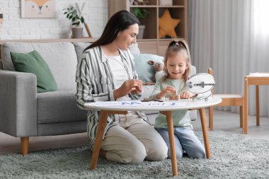 Ofisteki masada mektupları telaffuz eden küçük bir kız ve küpleri olan kadın konuşma terapisti.
