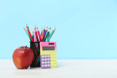 Mavi arkaplanda kırmızı elmalı kalem ve hesap makinesi var.