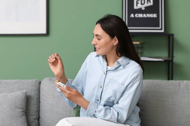 Evdeki kanepede glukometre kullanan şeker hastası genç bir kadın.