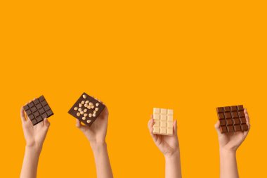 Sarı arka planda farklı çikolata çubukları olan kadın elleri.