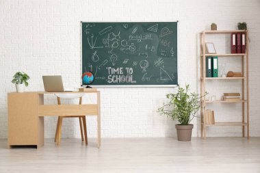 Aydınlık sınıfta dizüstü bilgisayarı ve tahtası olan öğretmenler masası.