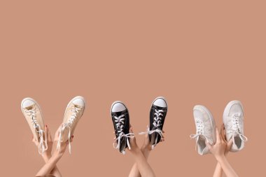 Bej arka planda farklı spor ayakkabıları olan kadın elleri.