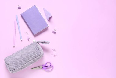 Kağıt uçak, kalem kutusu ve pembe arka planda farklı kırtasiye malzemeleri.