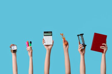 Mavi zemin üzerinde kırtasiye ve alarm saati olan birçok el