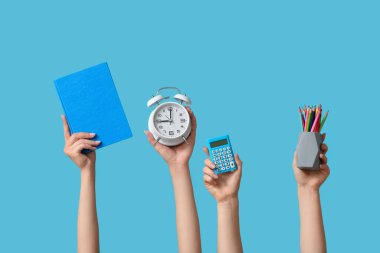 Mavi zemin üzerinde kırtasiye ve alarm saati olan birçok el