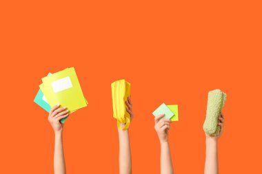 Kalem kutuları, yapışkan notlar ve turuncu arkaplan üzerine not defterleri olan birçok el.