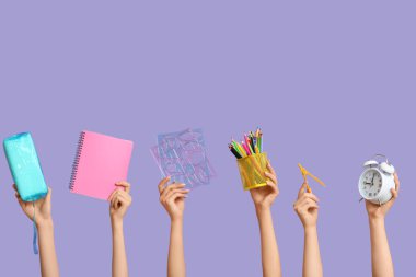 Kırtasiye malzemesi, çalar saat ve mavi arkaplanda not defteri olan birçok el.