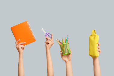 Kırtasiye malzemesi, defter ve kalem kutusu olan birçok el gri arkaplanda.