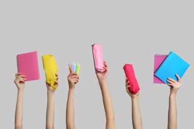 Gri arkaplan üzerinde defter, kırtasiye ve kalem kılıfları olan birçok el