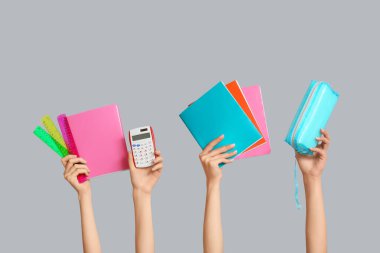 Gri arkaplan üzerine hesap makinesi, kırtasiye ve not defterleri olan birçok el