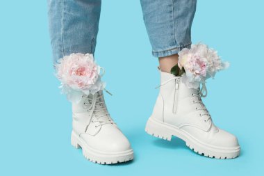 Mavi arka planda şakayık çiçekleri olan çizmeli genç bir kadının bacakları.