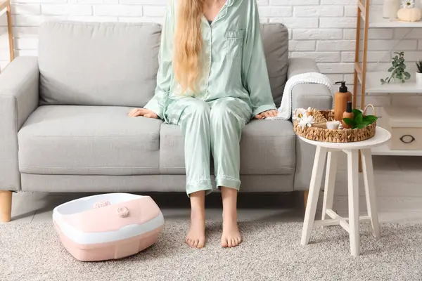 Masaj banyosu ve spa malzemeleri olan bir kadın evdeki kanepede oturuyor.