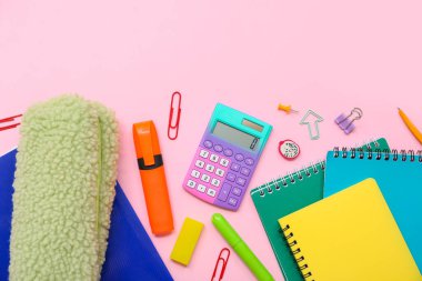 Hesap makineli okul gereçleri, not defterleri ve pembe arka planda işaretleyici. Üst görünüm