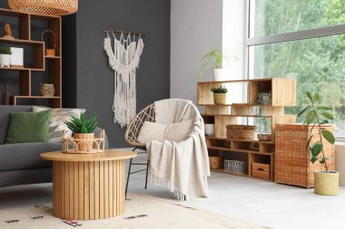 Şık oturma odasının içinde hasır sandalye, raf ve masa.