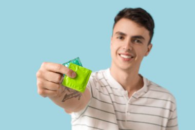 Mavi arka planda prezervatif gösteren genç adam, yakın plan.