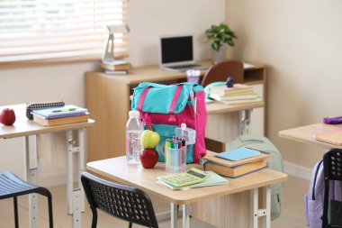 Sınıftaki masada su şişesi ve sırt çantalı elmalar.