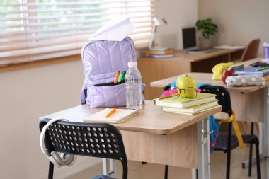 Sınıfta masada gözlüklü, kitaplı ve sırt çantalı bir elma.