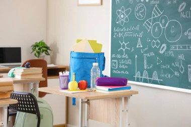 Okul kırtasiyeli elmalar, su şişesi ve sırt çantası sınıfta masanın üzerinde.