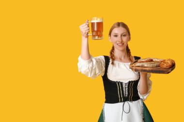 Güzel mutlu Ekim Festivali garsonu, birası ve sarı arka planda geleneksel yemekleri var.