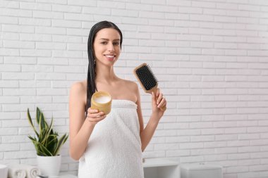 Bir kavanoz saç maskesi ve banyoda fırçası olan güzel, genç ve mutlu bir kadın.