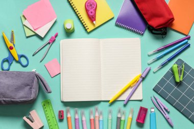 Turkuaz arka planda farklı kırtasiye malzemesi içeren boş bir defter