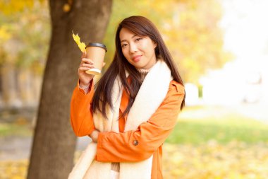 Güz parkında bir fincan kahveyle mutlu bir Asyalı kadın.