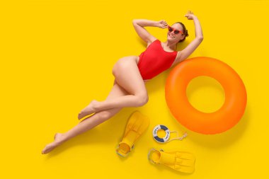 Yüzme yüzüklü ve yüzgeçli kadın turist sarı arka planda yatıyor.