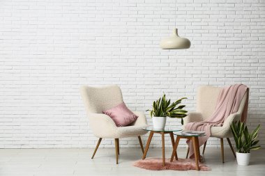 Koltuklar, masalar ve sansevieria bitkileri oturma odasının içindeki beyaz tuğla duvarın yanında.