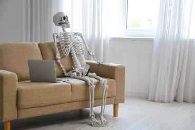 Oturma odasındaki kanepede dizüstü bilgisayarı olan iskelet.