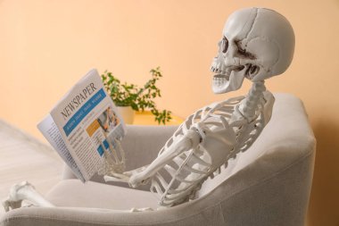 İskelet ve gazete oturma odasındaki bej duvarın yanındaki koltukta oturuyor.