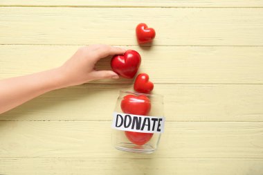 El, kelime donatımlı kavanoz ve sarı tahta arka planda kırmızı kalpler. Bağış konsepti