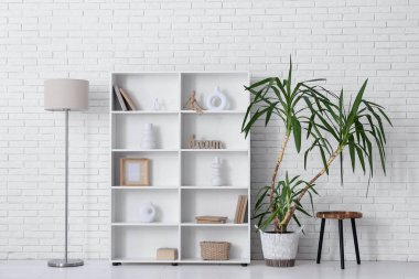 Raflama ünitesi, standart lamba ve beyaz tuğla duvarın yanındaki bitki.