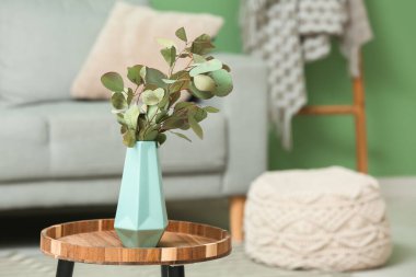 Oturma odasının içindeki masada okaliptüs dalları olan mavi vazo, yakın plan.