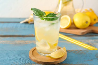 Mavi ahşap masada fesleğen yapraklı bir bardak taze limonata.