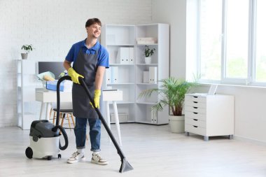 Ofisinde modern elektrik süpürgesi olan genç erkek hademe.