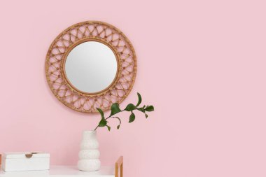 Raflarda yeşil dalı olan vazo ve pembe duvarda yuvarlak ayna, yakın plan.