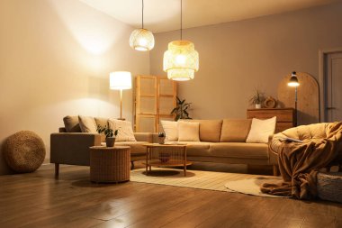 Şık oturma odasının içinde rahat gri koltuklar, sehpa ve akşam lambaları var.