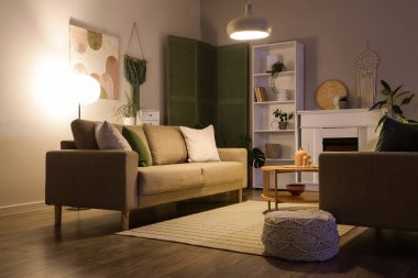 Gri koltukları, kahve masası, şöminesi ve gece lambaları olan şık bir oturma odası.