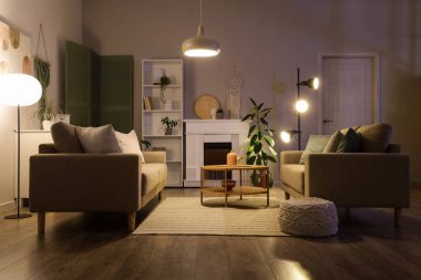 Gri koltukları, kahve masası, şöminesi ve gece lambaları olan şık bir oturma odası.