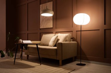 Şık oturma odasının içinde rahat bir kanepe, sehpa ve akşam lambaları var.