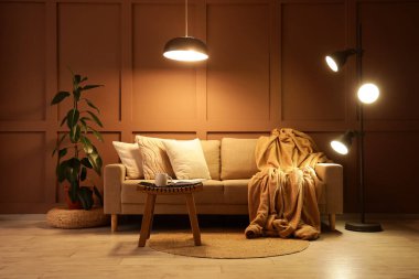 Şık oturma odasının içinde rahat bir kanepe, sehpa ve akşam lambaları var.