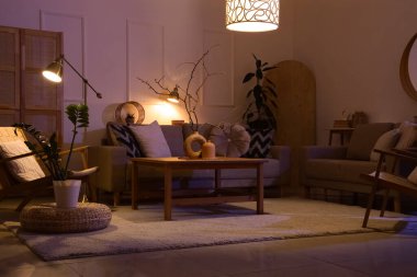 Lüks oturma odasının içinde rahat gri koltuklar, koltuklar, sehpa ve geceleri parlayan lambalar.