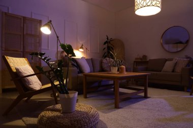 Şık oturma odasının içinde rahat gri koltuklar, koltuk, sehpa ve geceleri parlayan lambalar.