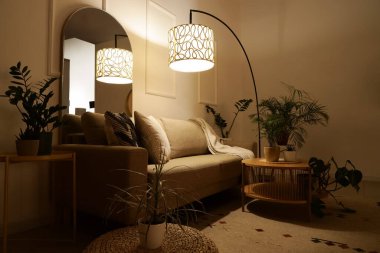 Lüks oturma odasının içinde rahat gri kanepe, sehpa, ev bitkileri ve akşam lambaları.