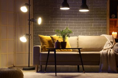 Şık oturma odasının içinde rahat bir kanepe, sehpa ve akşam lambaları var.