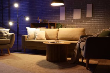 Şık oturma odasının içinde rahat bir kanepe, sehpa, koltuklar ve geceleri parlayan lambalar.