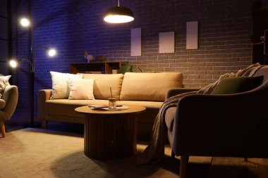 Şık oturma odasının içinde rahat bir kanepe, sehpa, koltuk ve geceleri parlayan lambalar.