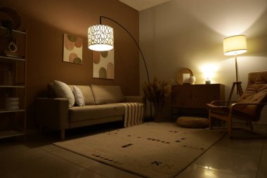 Şık oturma odasının içinde rahat bir kanepe, koltuk ve akşam lambaları var.